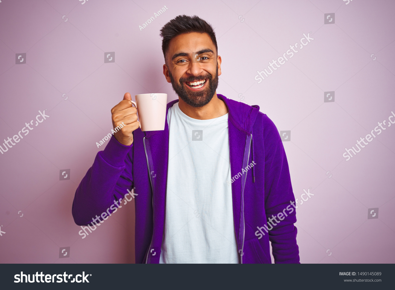 Indian man wearing purple sweatshirt drinking cup of coffee over isolated pink background with a happy face standing and smiling with a confident smile showing teeth #1490145089