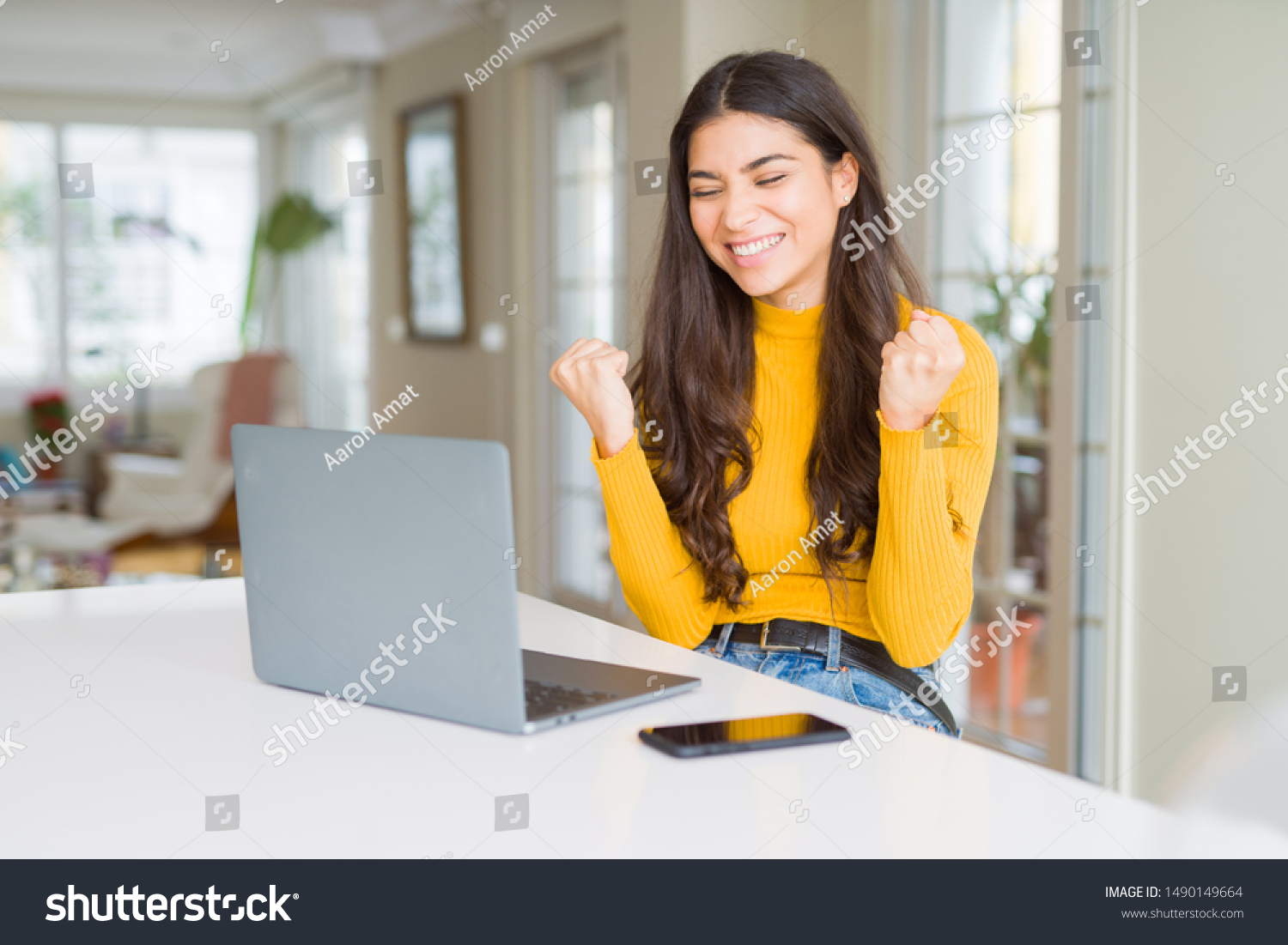 Young woman using computer laptop very happy and excited doing winner gesture with arms raised, smiling and screaming for success. Celebration concept. #1490149664