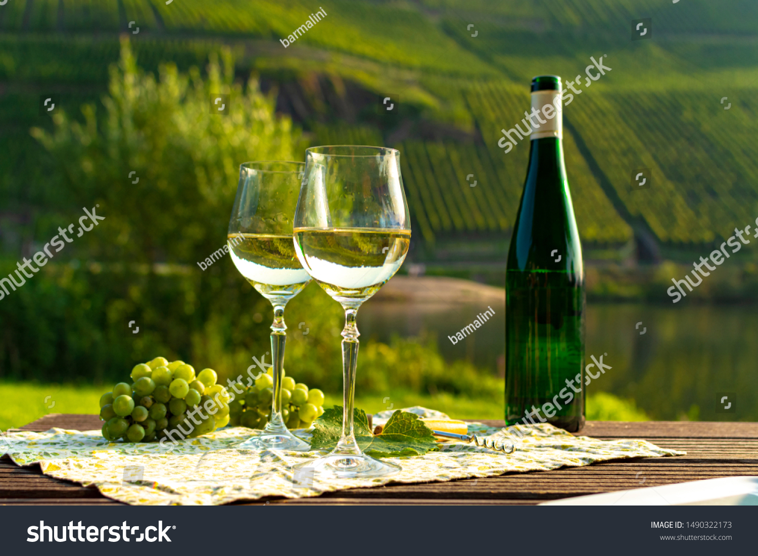 Famous German quality white wine riesling, produced in Mosel wine regio from white grapes growing on slopes of hills in Mosel river valley in Germany, bottle and glasses served outside in Mosel valley #1490322173