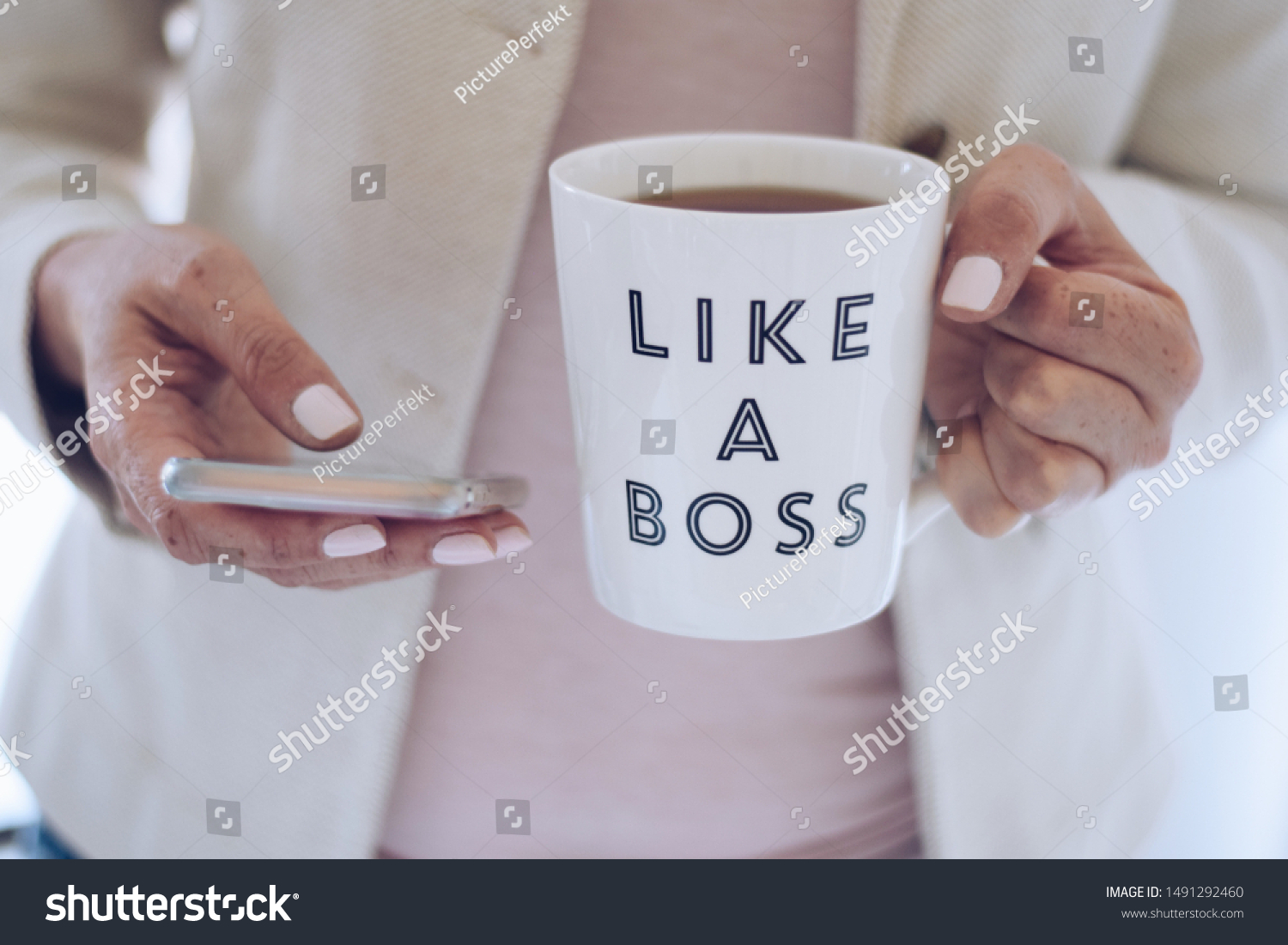 Professional woman using mobile phone and holding a cup that says LIKE A BOSS #1491292460