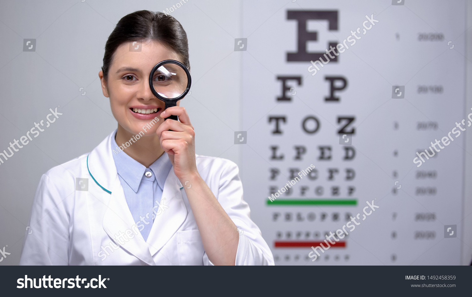Smiling optometrist looking through magnifying glass and smiling, sight test #1492458359