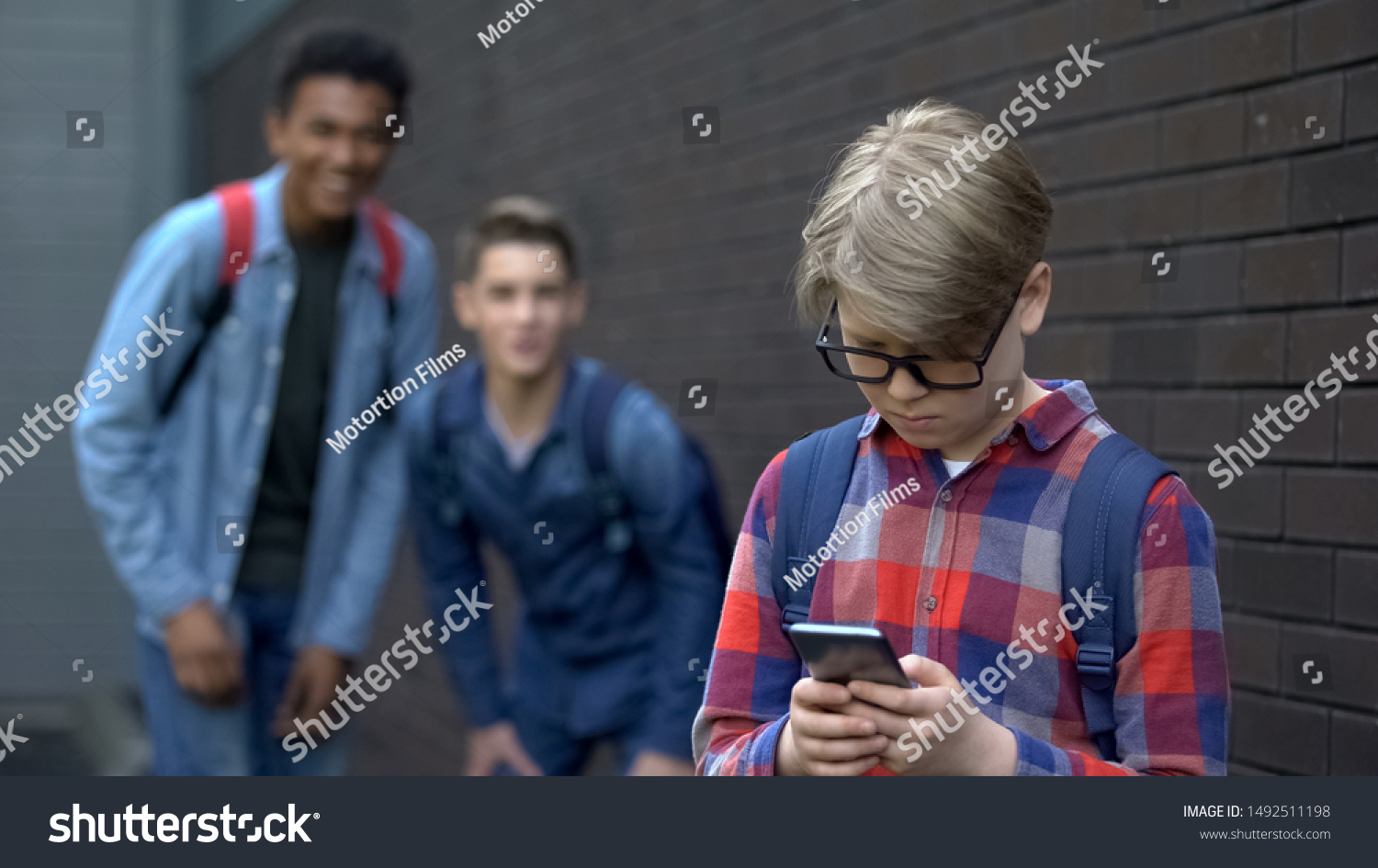Junior student reading offensive post in phone, boys mock behind, cyberbullying #1492511198