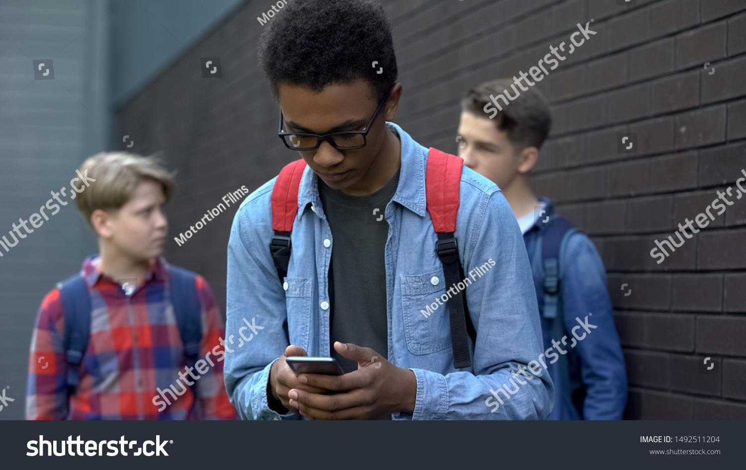 Black student reading offensive post in phone, boys mock behind, cyberbullying #1492511204
