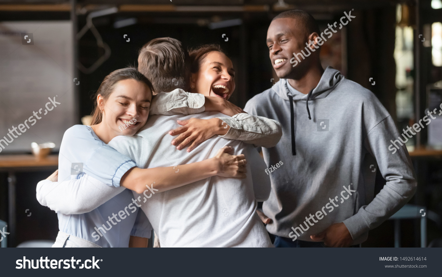 Excited diverse friends embrace greeting male buddy coming at meeting in cafe, multiracial students group hugging guy laughing say hello welcoming at students reunion, multi ethnic friendship concept #1492614614