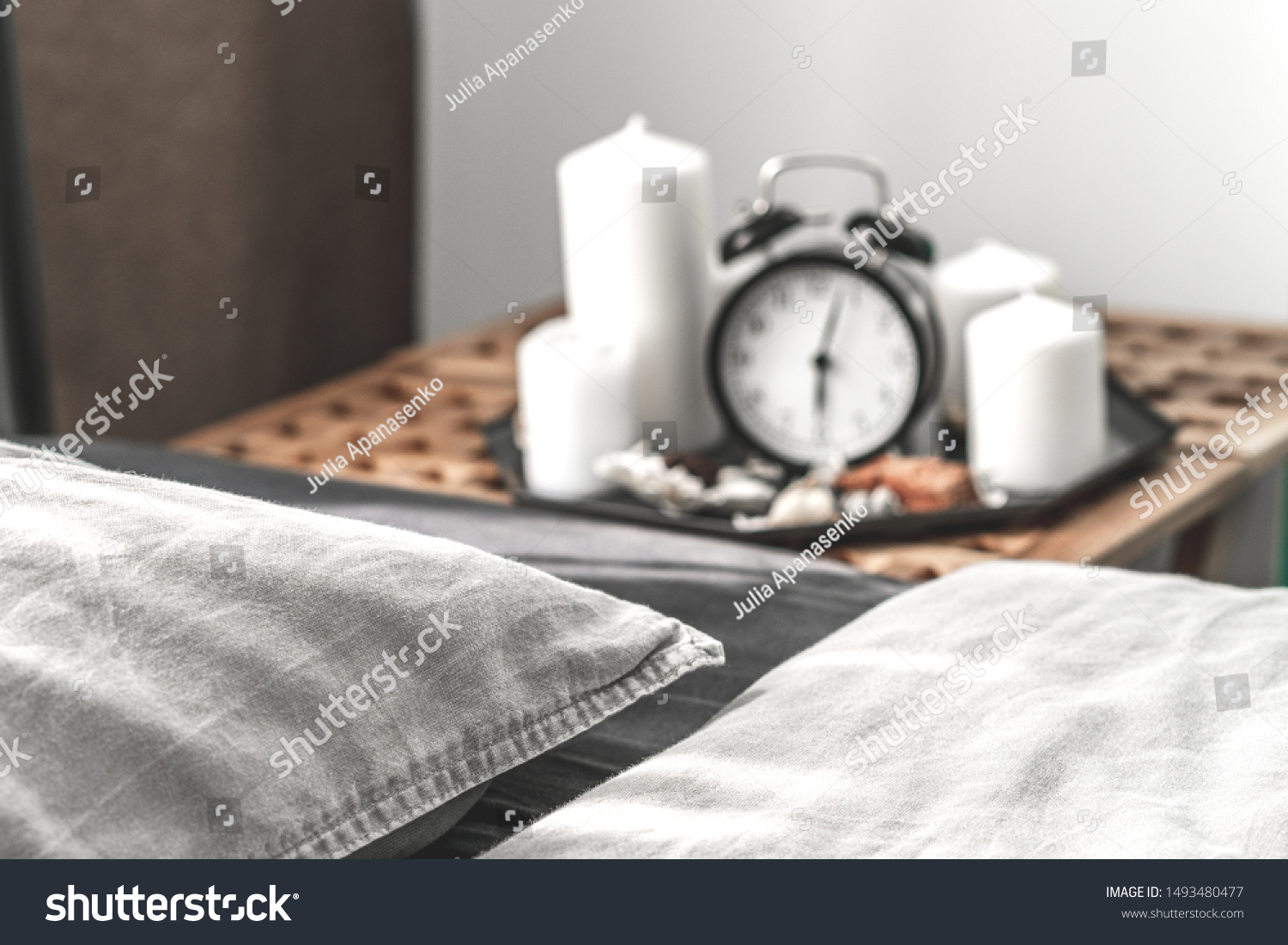 Cozy gray bedroom interior with comfortable bed near the wooden night table with candle, alarm clock and dried flowers. Cozy atmosphere at home. Warming up the cold evenings. Vintage furniture.  #1493480477