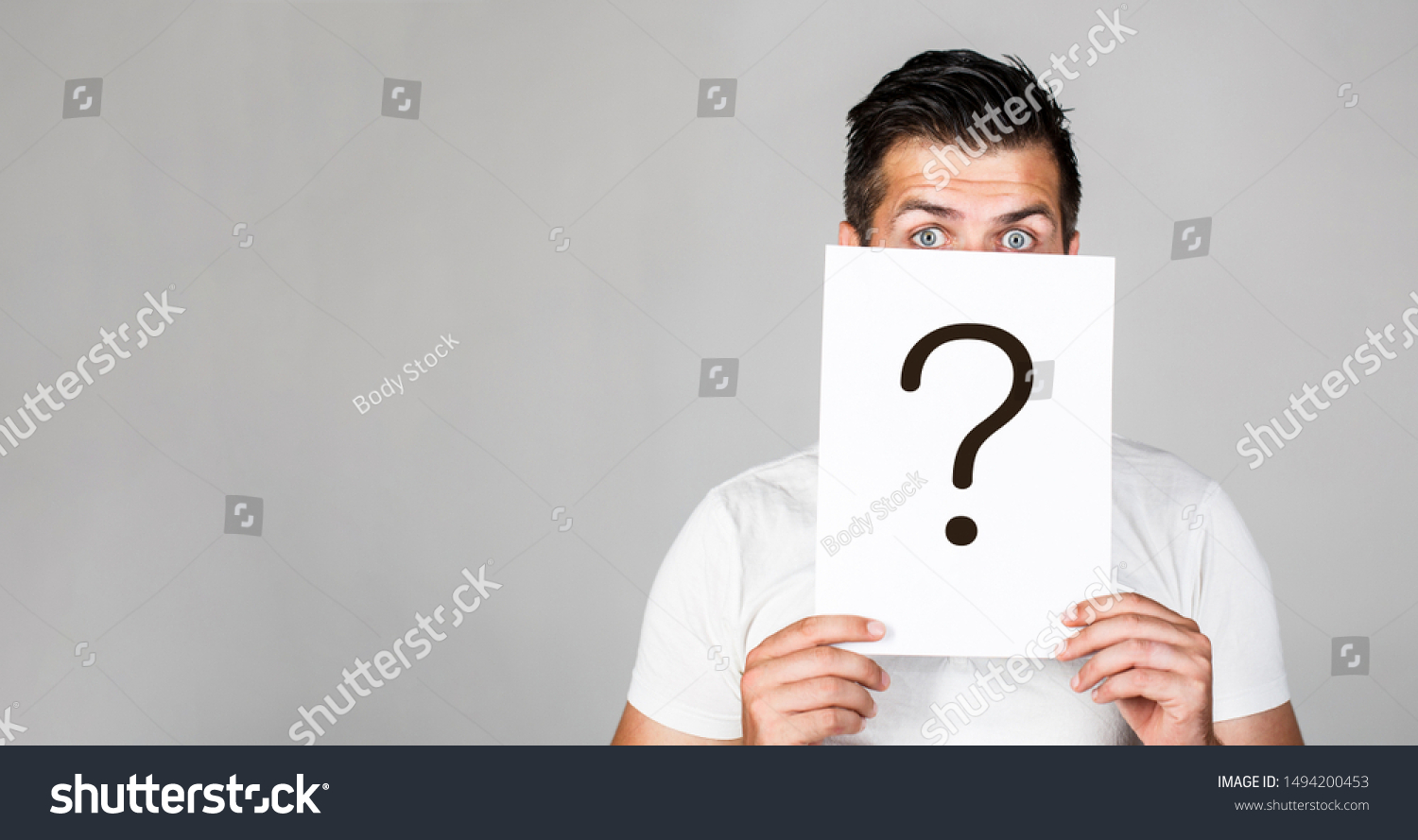Portrait of man, peeking behind of interrogation symbol. Question mark, symbol. Pensive male. Man a question. Doubtful man holding Question Mark. Problems and solutions. Copy space. #1494200453