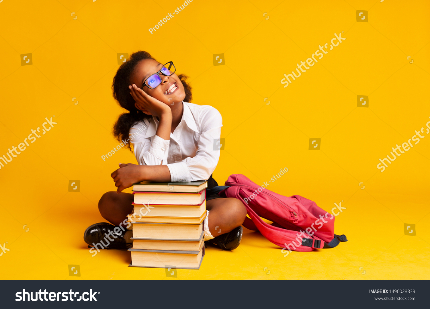 Cheerful African American Schoolgirl Dreaming Sitting At Book Stack Over Yellow Background In Studio. Copy Space #1496028839