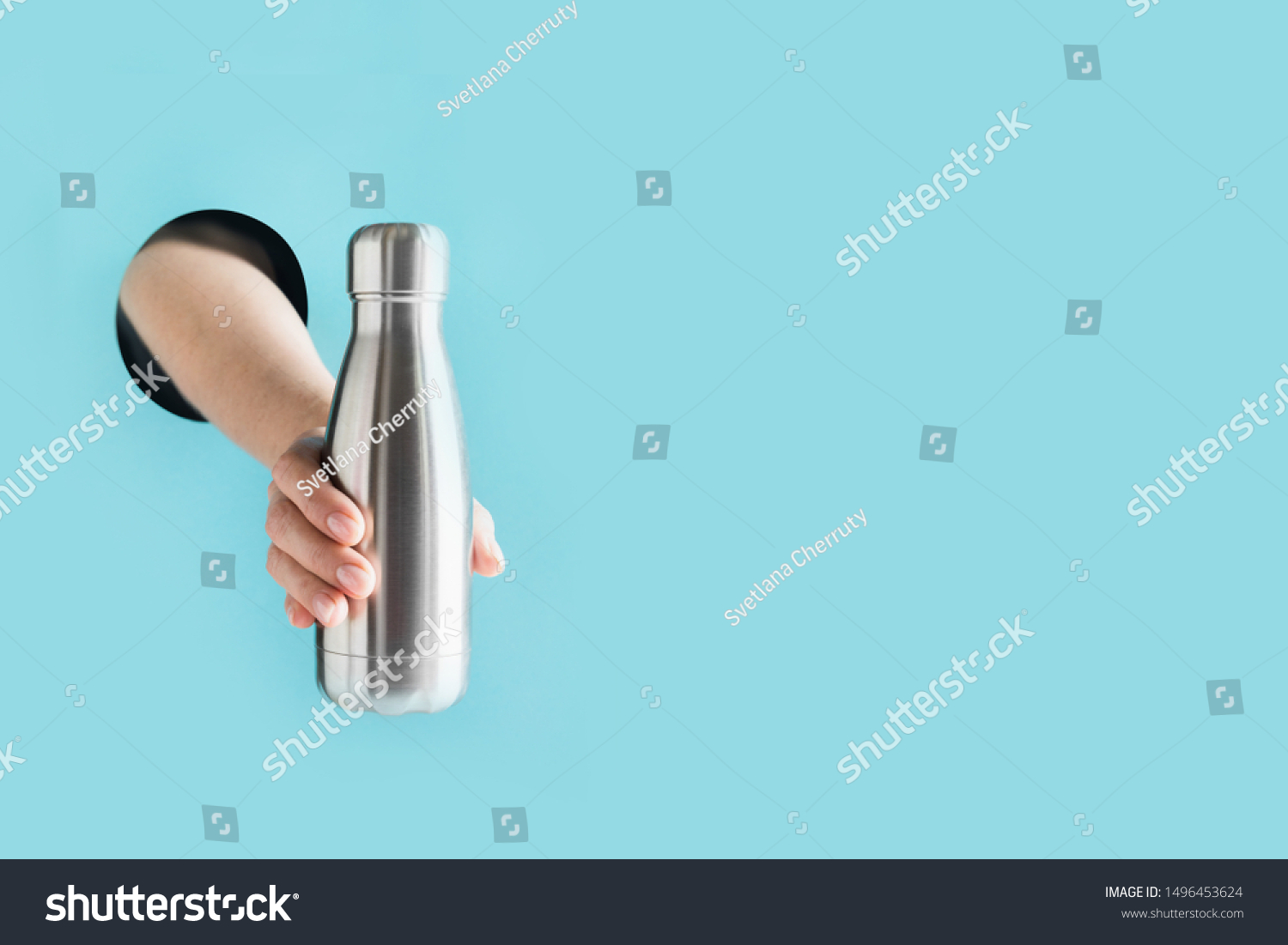 Reusable metal bottle for drinks in female hand through the hole in paper. Individual use. Save the planet. Zero waste concept. Plastic free. #1496453624
