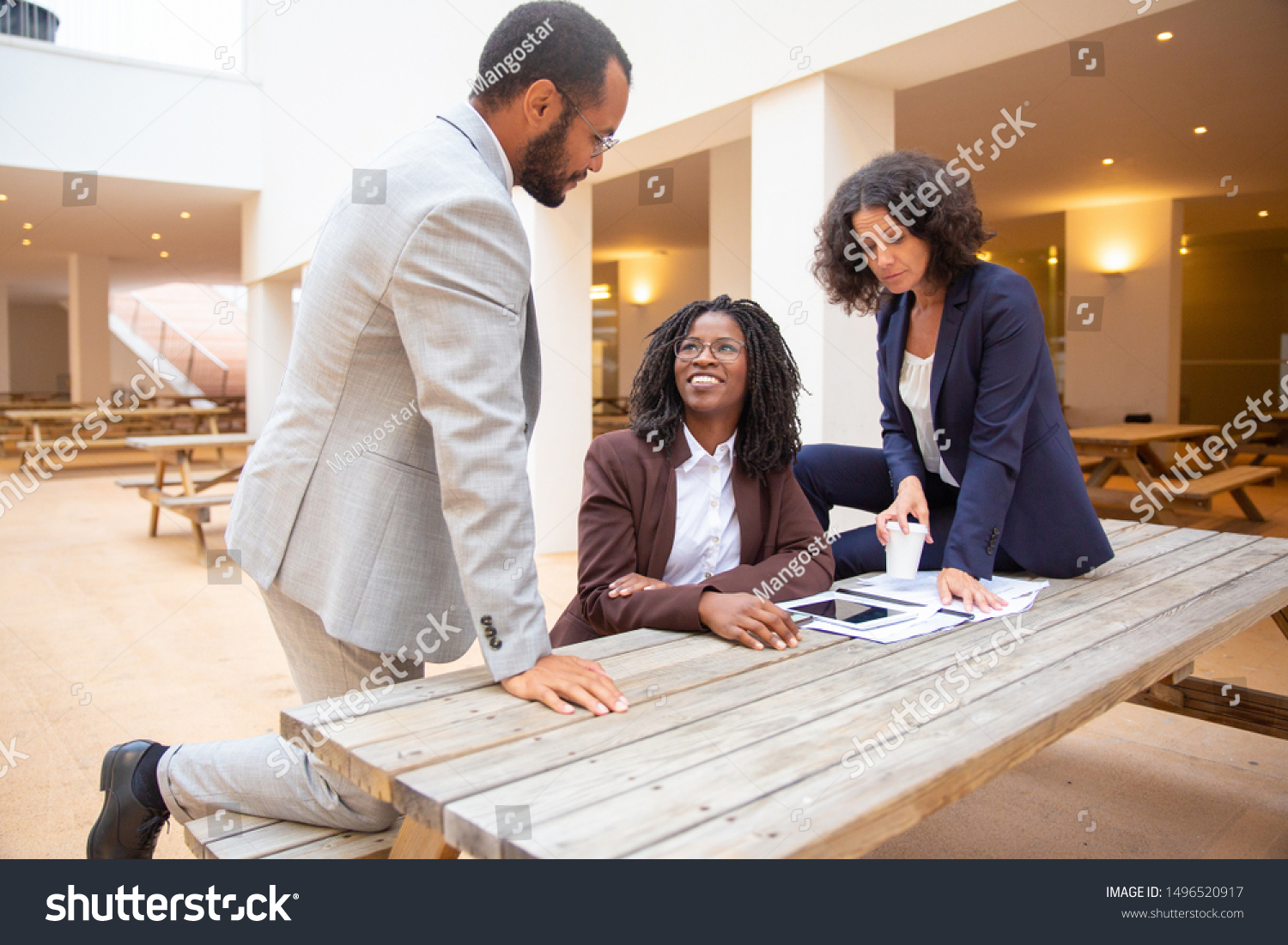 Successful diverse team working on project in outdoor cafe. Business man an women gathering at table with papers and tablet and talking outside. Teamwork outside concept #1496520917