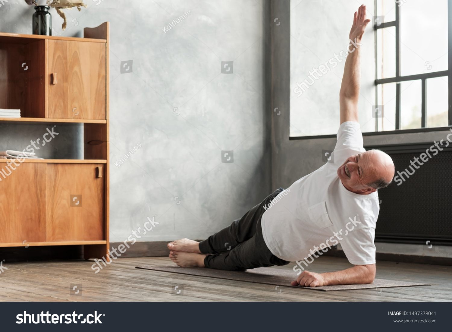 Cheerful senior hispanic man doing a side plank exercise at living room. Doing yoga at home at old age. #1497378041
