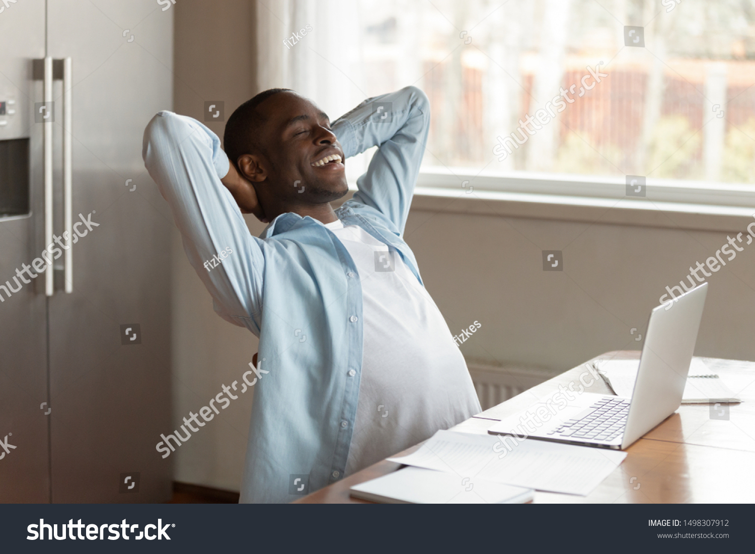 Calm relaxed african American male worker sit at table distracted from work dreaming or visualizing, peaceful dreamy biracial man lean back relax in chair with eyes closed smiling thinking of success #1498307912