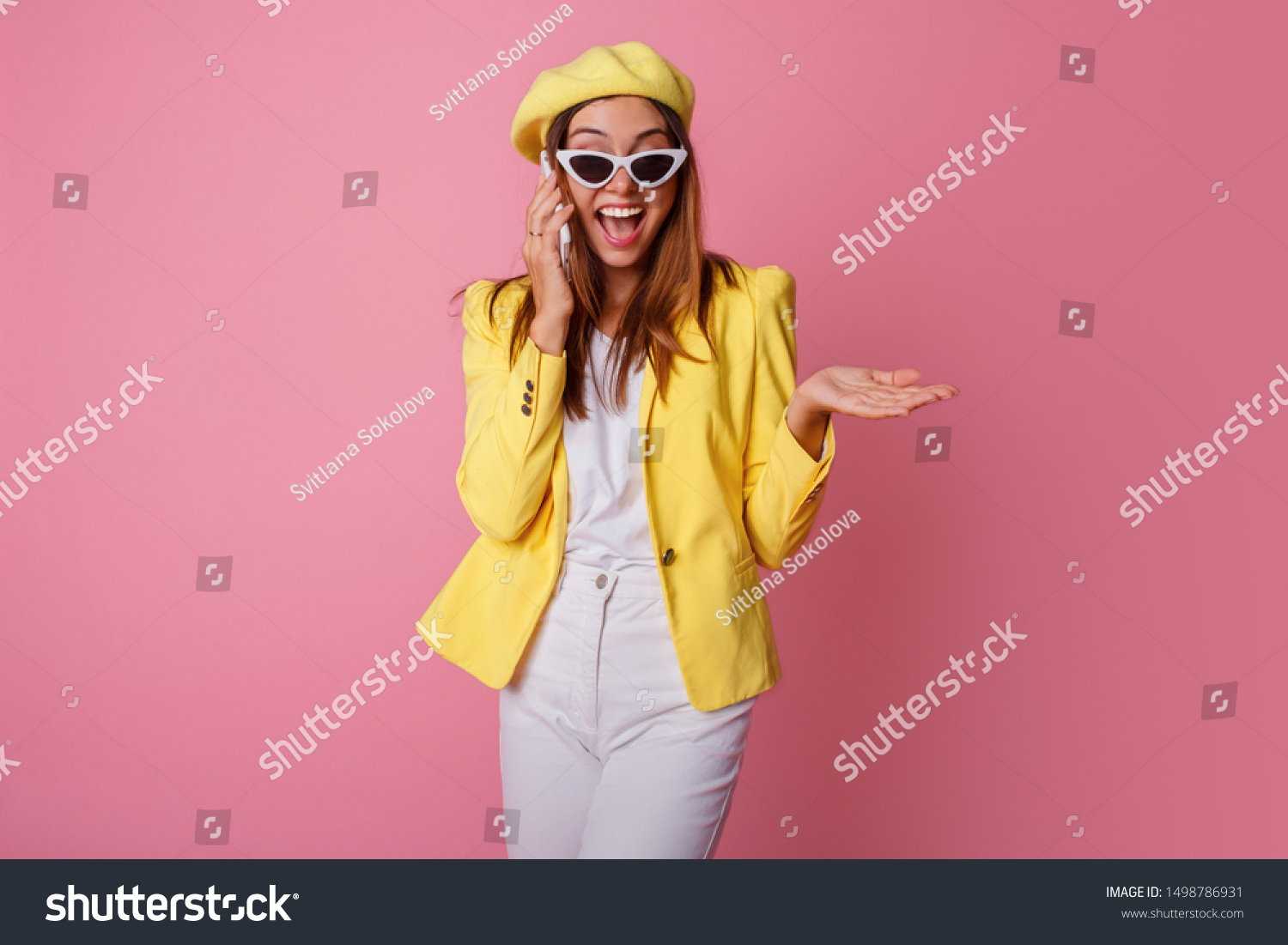 Stylish business woman talking by mobile phone with surprise emotions. Wearing yellow jacket and beret, standing over pink background. #1498786931