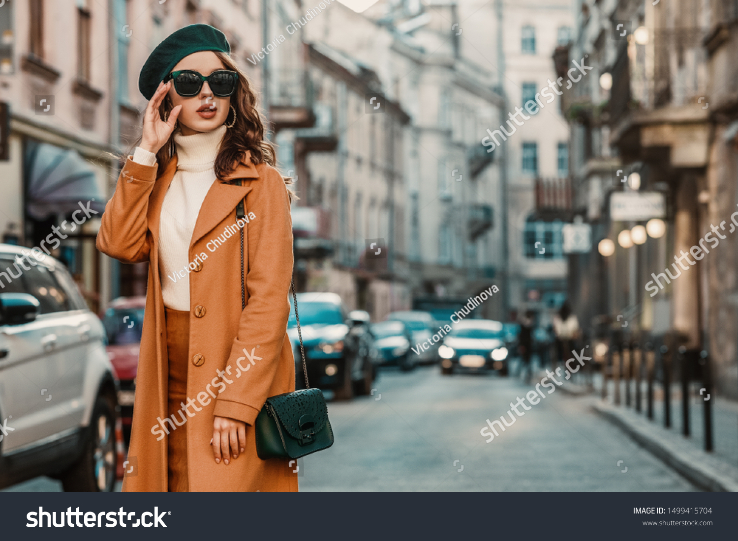 Outdoor autumn portrait of young elegant fashionable woman wearing trendy sunglasses, camel color coat, turtleneck, with textured leather shoulder bag, walking in street of European city. Copy space #1499415704