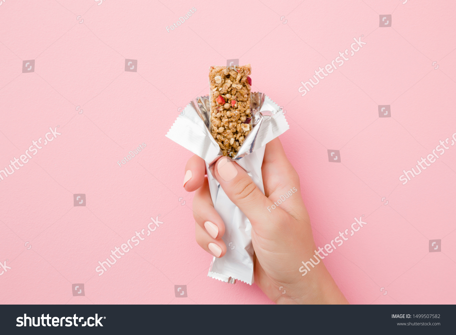 Young woman hand holding cereal bar on pastel pink table. Opened white pack. Closeup. Sweet healthy food. #1499507582