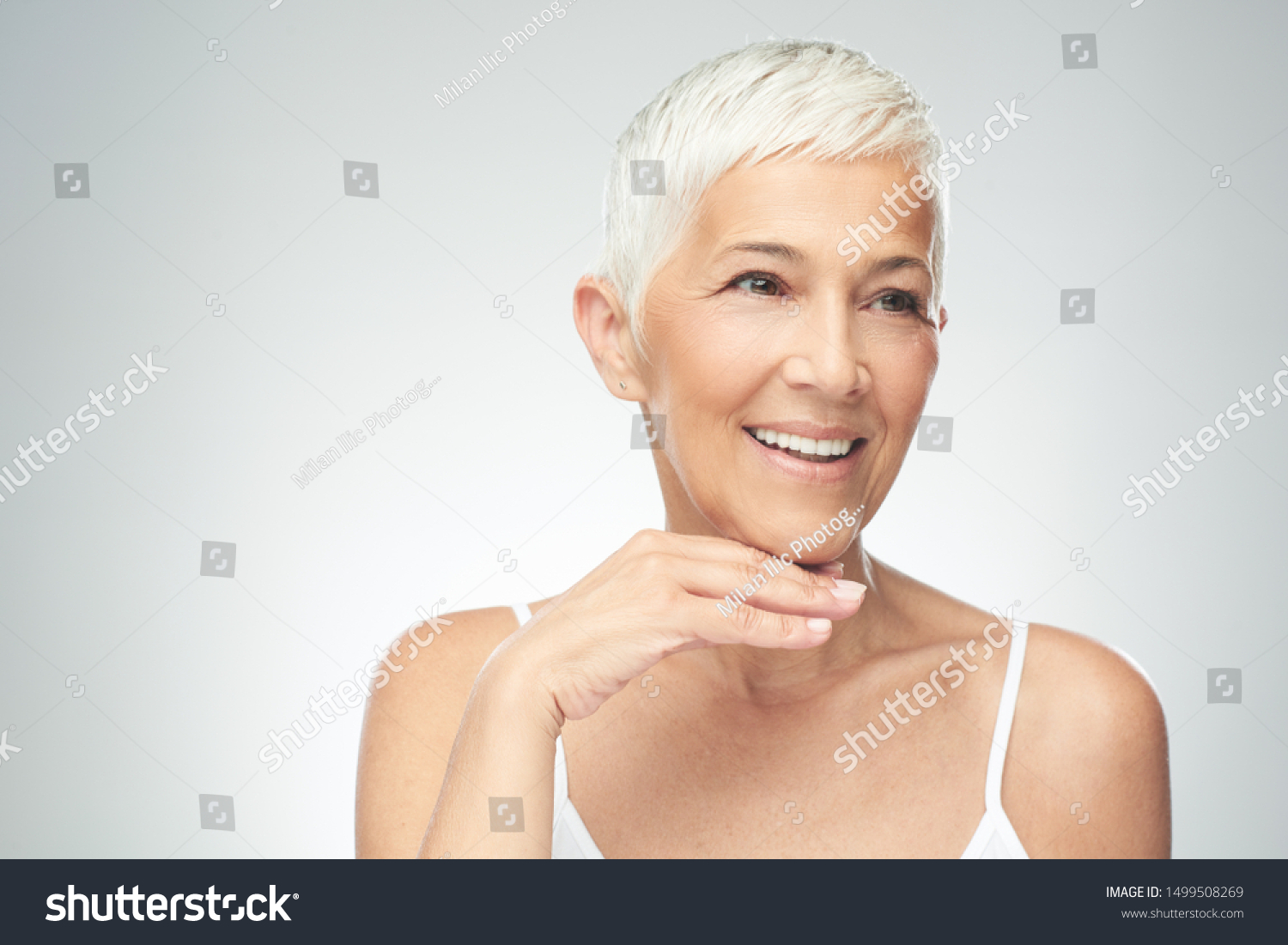Beautiful smiling senior woman with short gray hair posing in front of gray background. Beauty photography. #1499508269