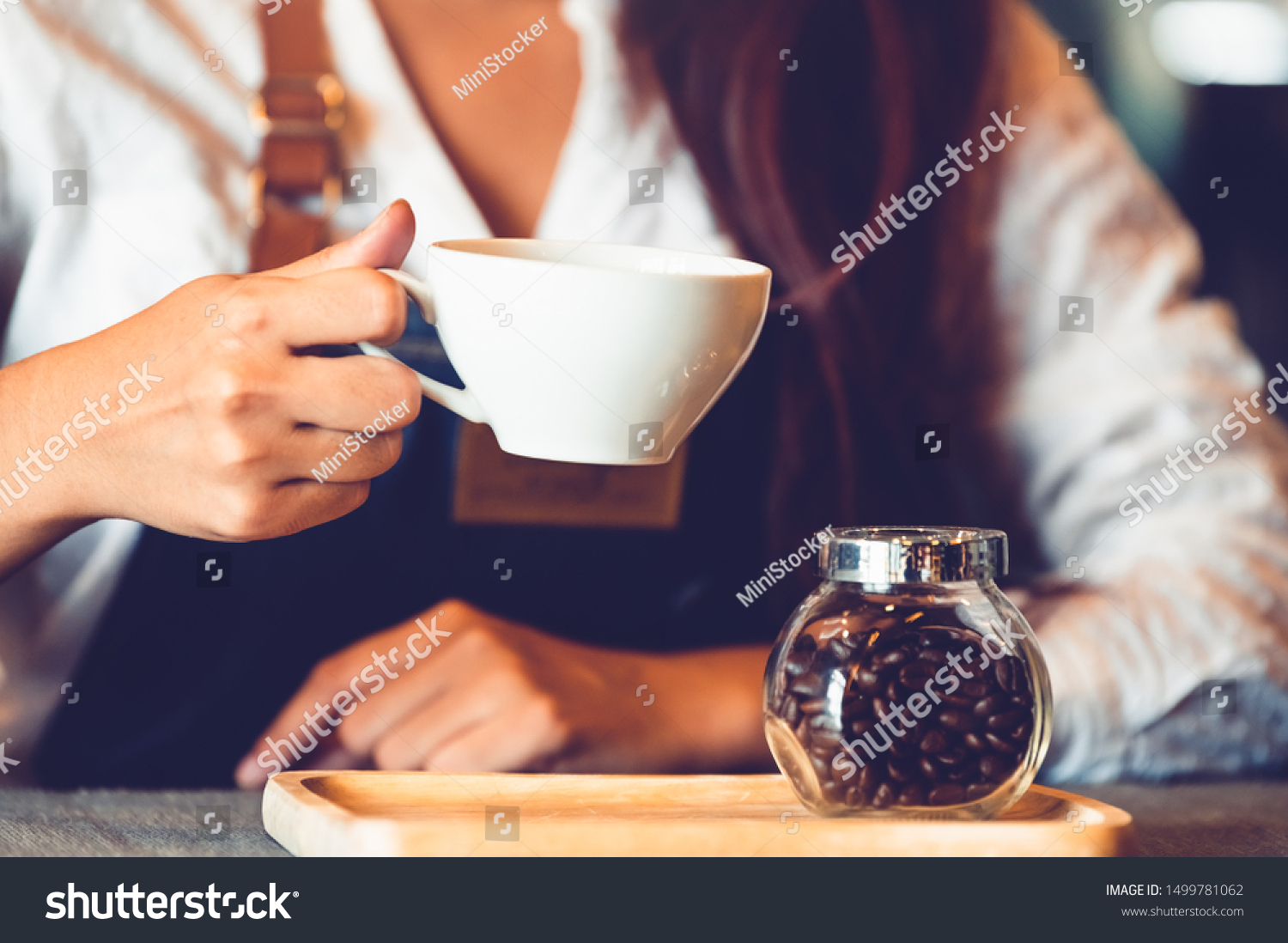 Closeup of professional female barista hand making and holding white cup of coffee. Happy young woman at counter bar in restaurant background. People lifestyles and Business occupation concept #1499781062