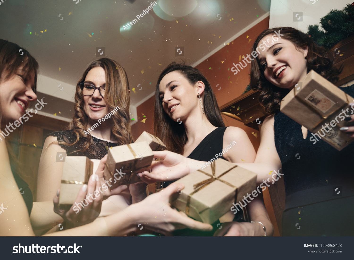 Four girlfriends celebrate New Year or Christmas by the fireplace. Laugh and give gifts to each other #1503968468