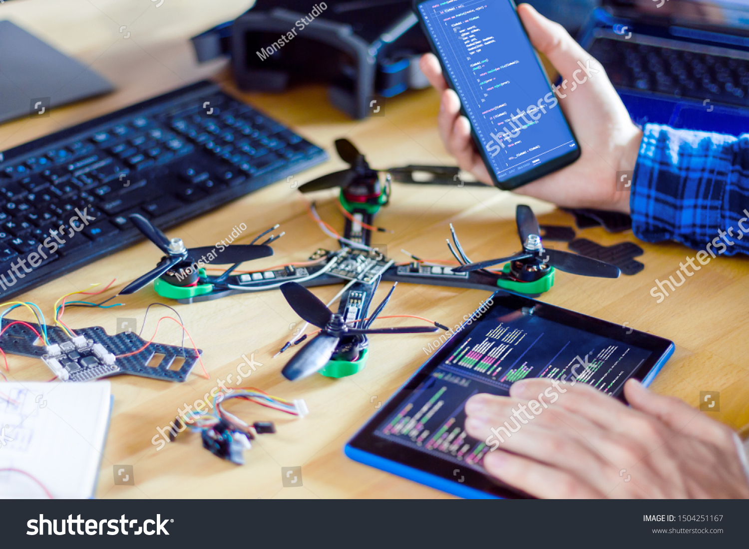 Closeup programmer hand holding smartphone and tablet with program code of software on screen for controlling FPV - first person view drone. Building quadcopter from kit with microcontrollers. #1504251167