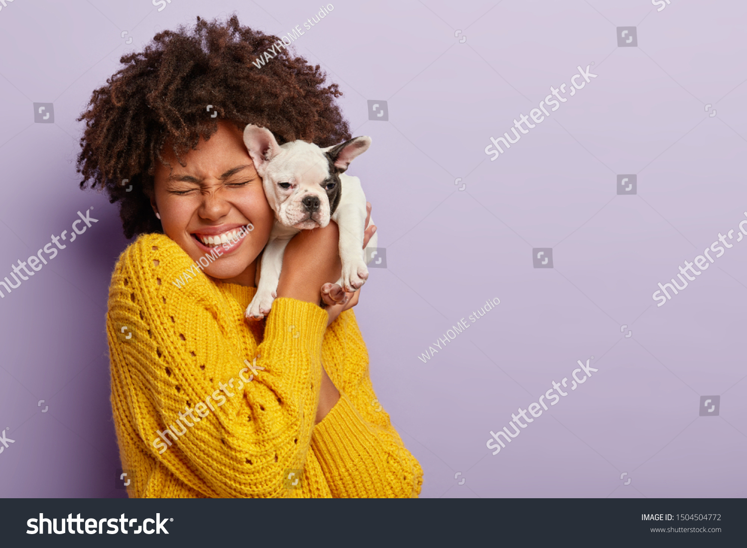 Dog owner and her pet. Happy ethnic curly girl holds cute little puppy near face, expresses love and care to domestic animal, buys dog of favourite breed, laughs, has eyes closed with pleasure #1504504772
