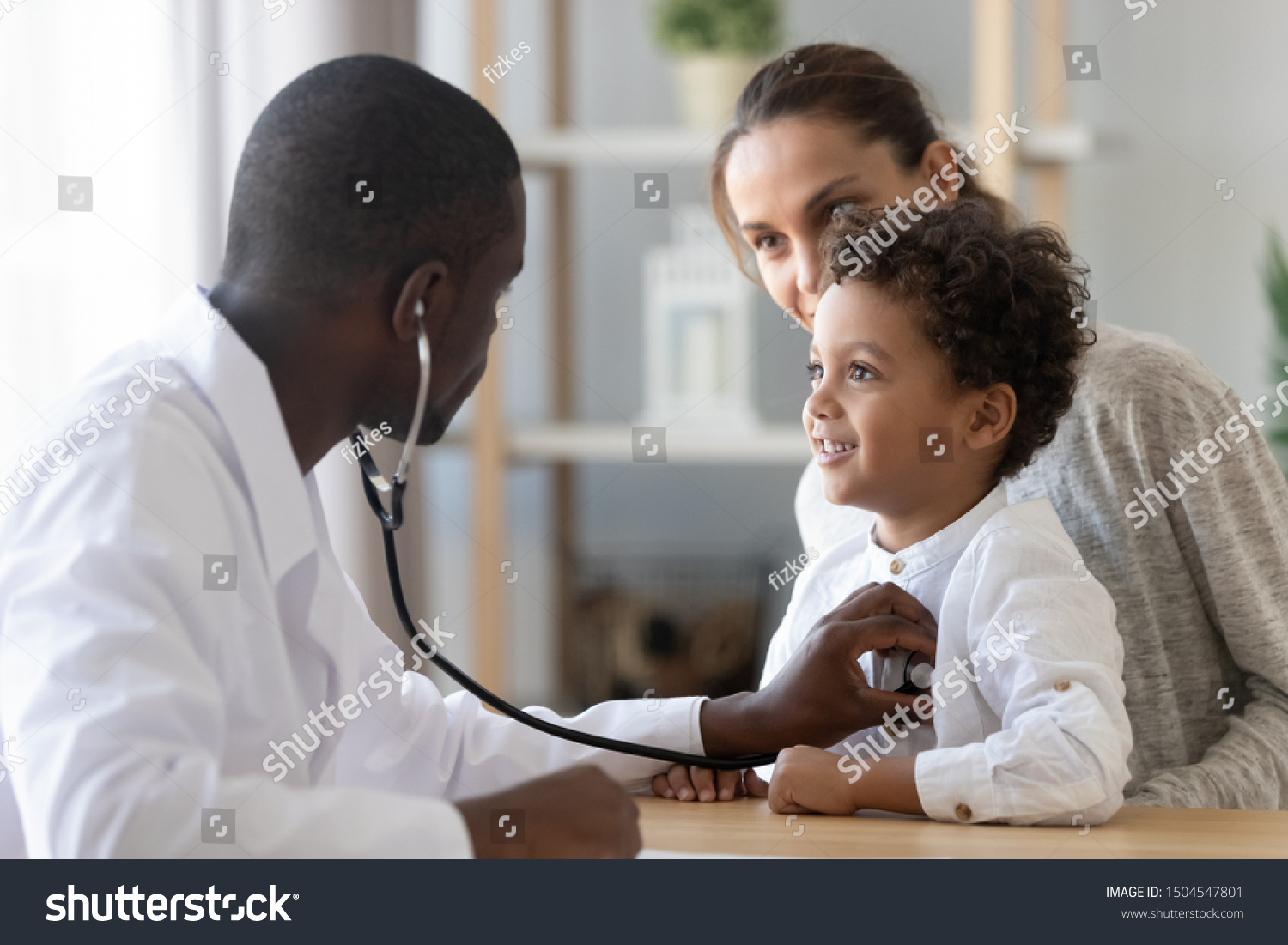 African American male pediatrician with stethoscope listening to lung and heart sound of little boy sitting on mother lap, physician checkup at home or in hospital, children medical insurance care #1504547801