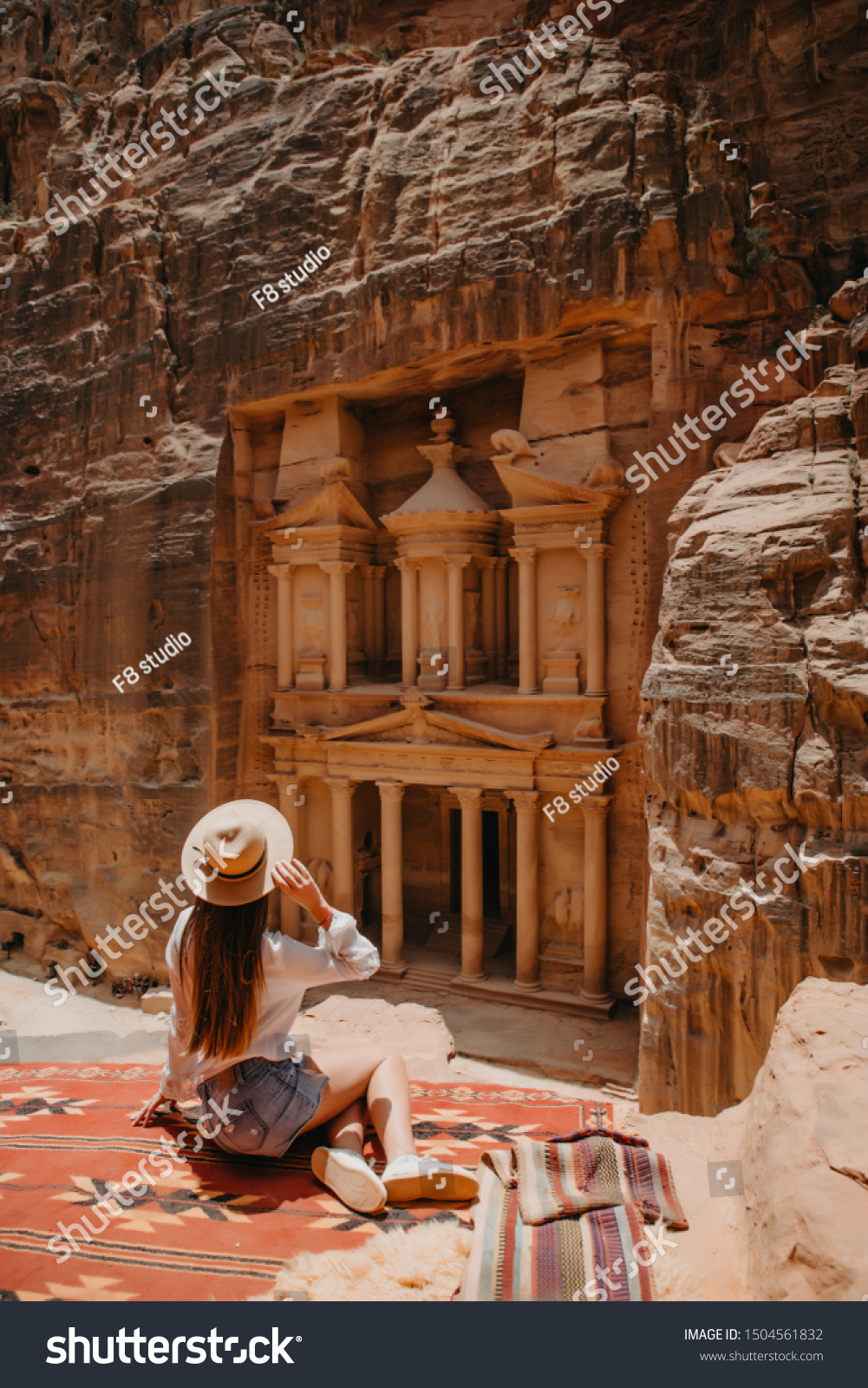 Aerial view of young woman tourist sitting on a cliff after reaching the top, Al Khazneh in the ancient city of Petra, Jordan, UNESCO World Heritage Site #1504561832