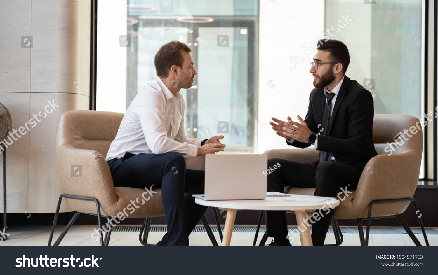 Middle eastern and caucasian ethnicity businessmen seated on armchair in modern office talking solve common issues, banker telling to client regarding bank services make recommendations and consulting #1504571753