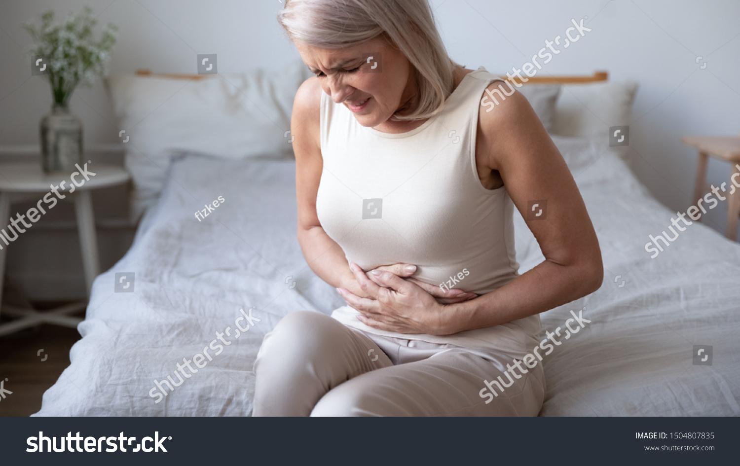 Unhealthy mature woman holding belly, feeling discomfort, health problem concept, unhappy older female sitting on bed, suffering from stomachache, food poisoning, gastritis, abdominal pain, climax #1504807835