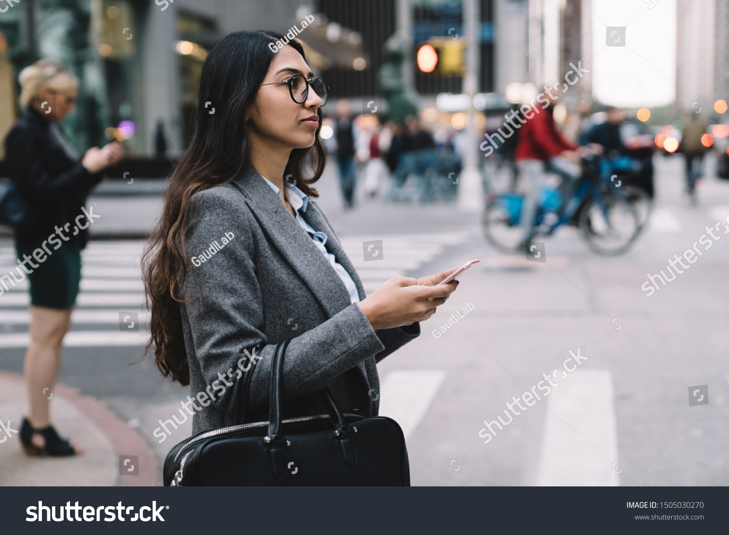 Side view of young businesswoman in office wear and glasses using mobile phone while crossing street in New York City  #1505030270