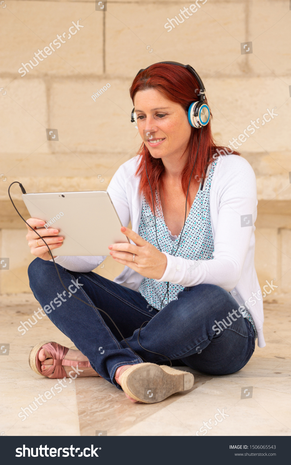 Pretty smiling redhead woman sitting on the floor listening to music or watching a movie on a touch pad #1506065543