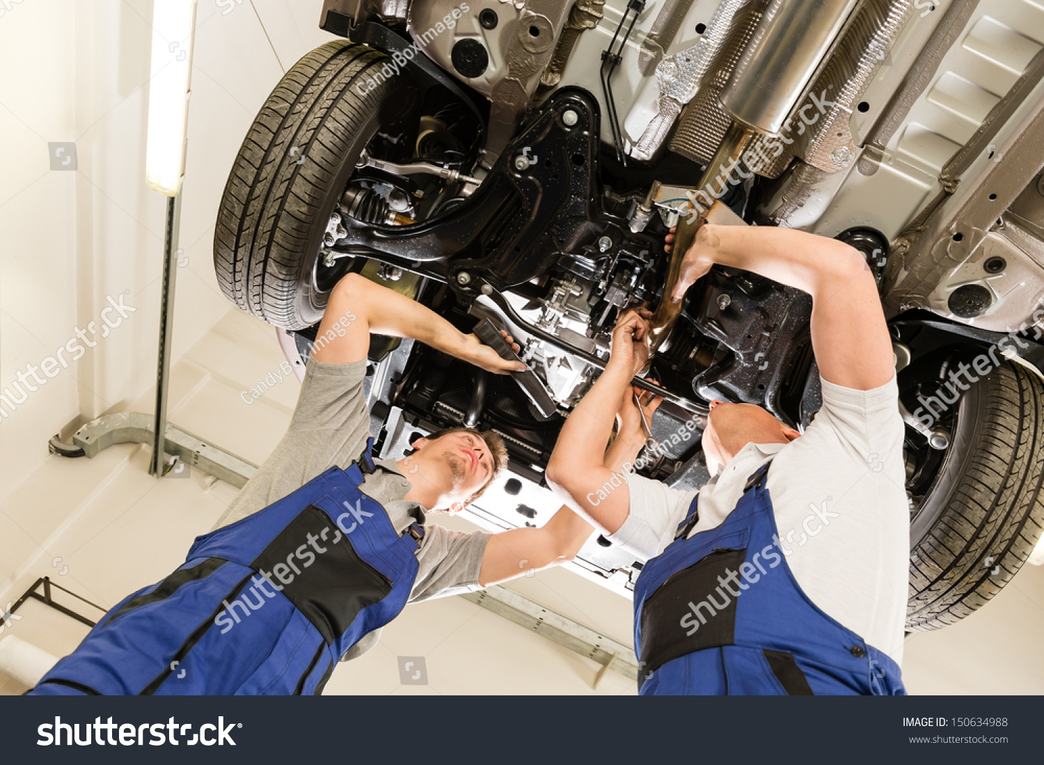 Auto mechanics working underneath a lifted car #150634988