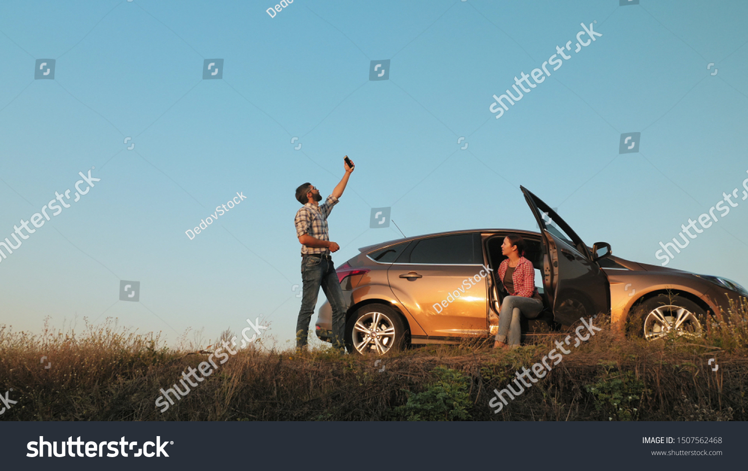 Man and woman traveling by car catches a phone signal while standing on the side of the road #1507562468