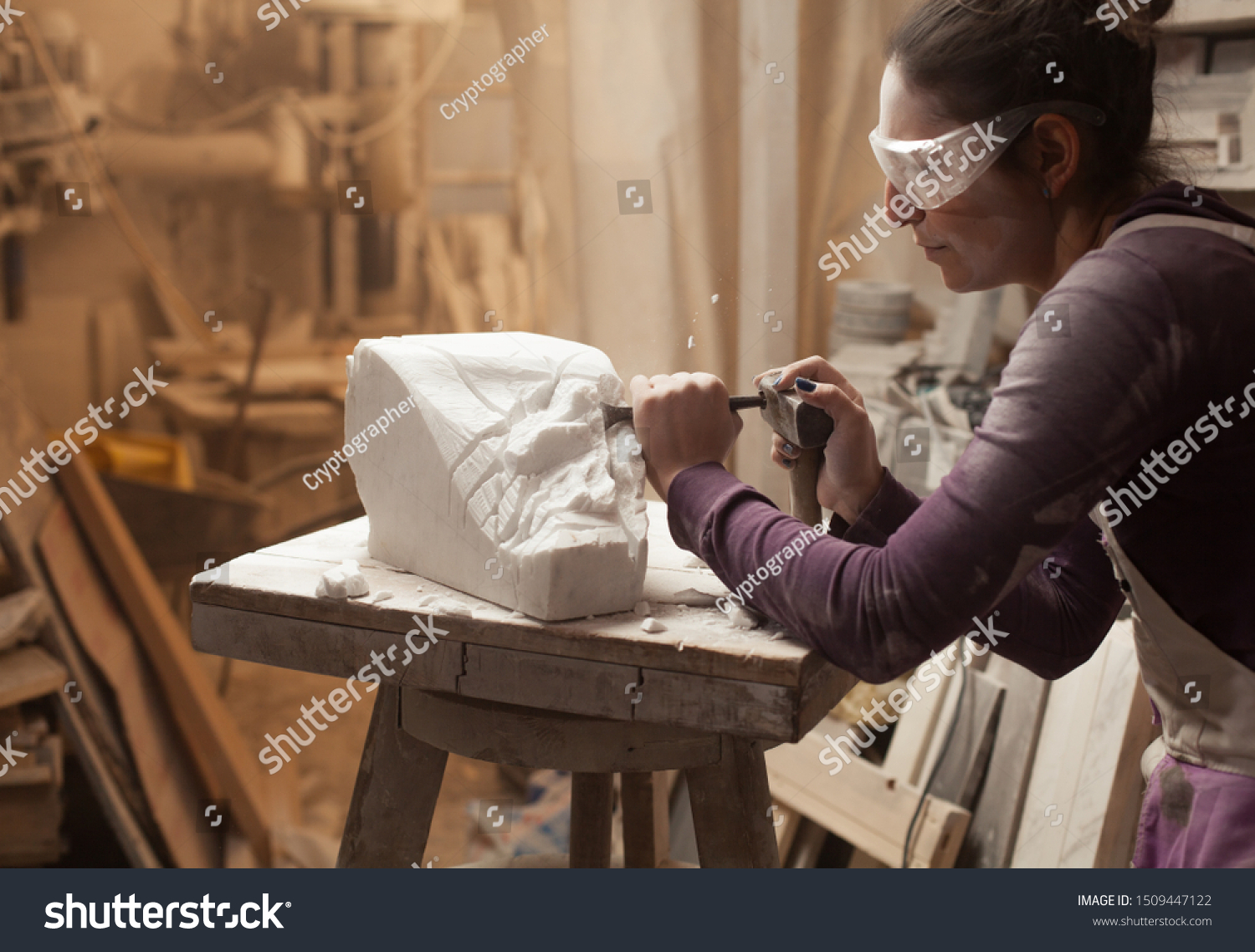 Female sculptor at work in a workshop, using hammer and chisel to sculpt a piece of white marble stone, debris and particles flying around, stonemasonry and stonecraft, copy space #1509447122