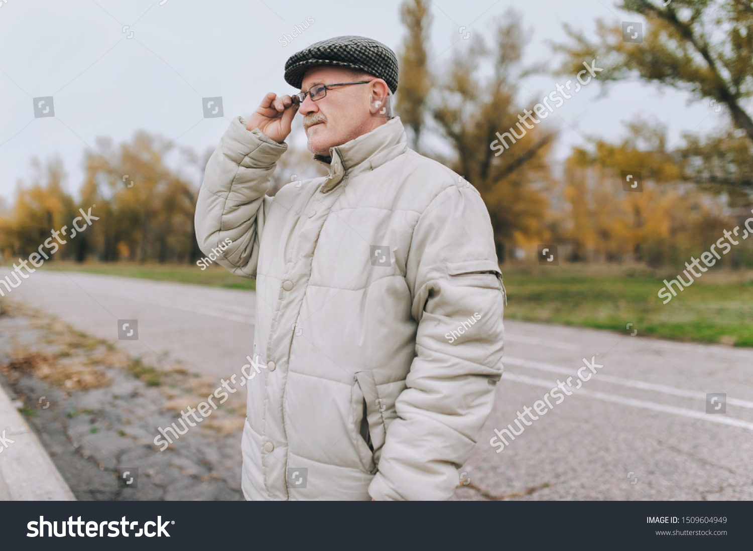 An old man in a jacket and a cap holds glasses in his hand and looks into the distance. The concept of retirement age and poor vision. Hyperopia, myopia. #1509604949