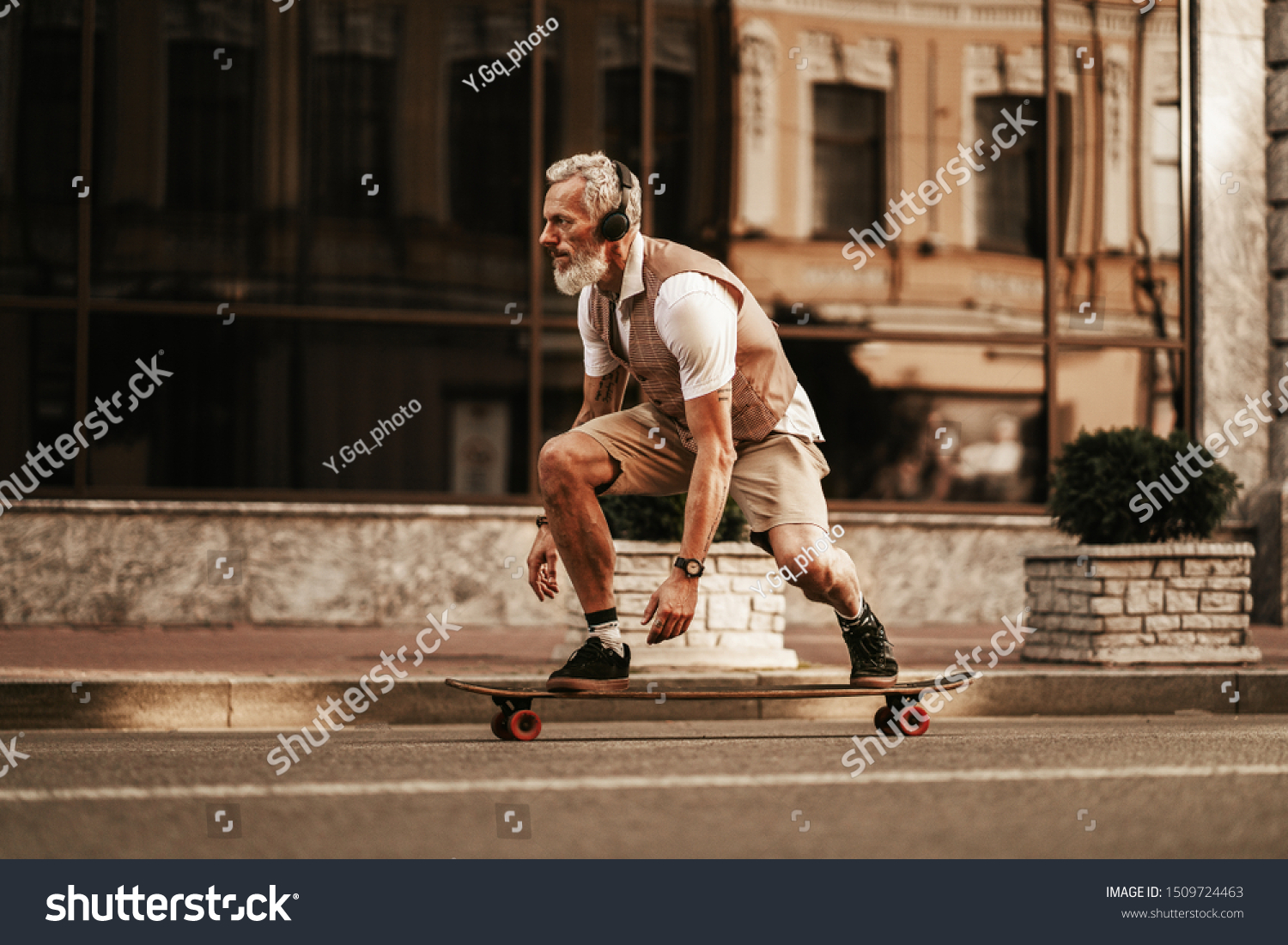 Portrait of bearded hipster man in white shirt on city street. Stylish happy model ride on longboard near road on buildings background #1509724463