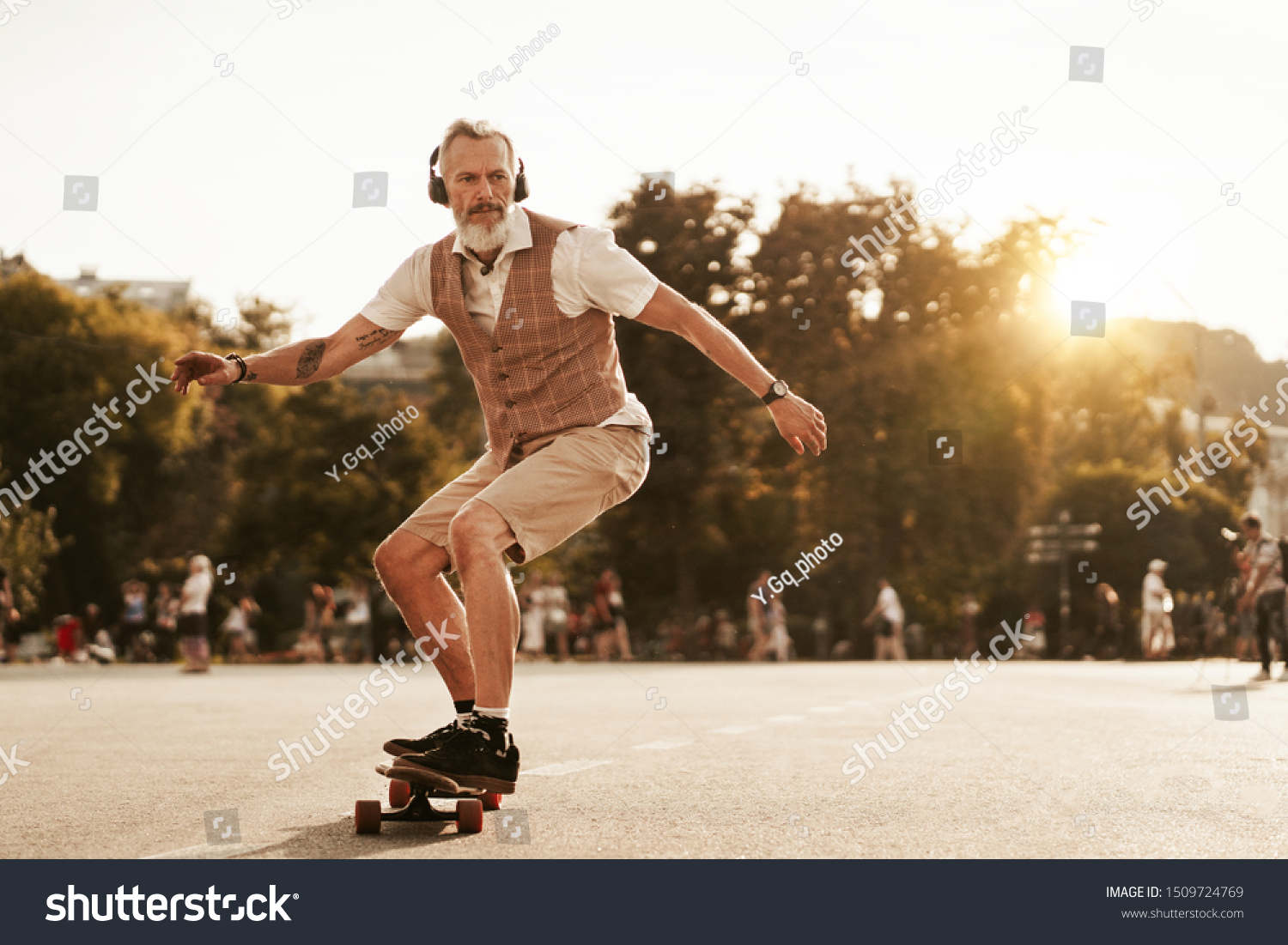 Skater posing in sunset evening on city street. Stylish hipster man with longboard ride near road on buildings background. Portrait of sport male model in urban style. Traveler. Tourist #1509724769