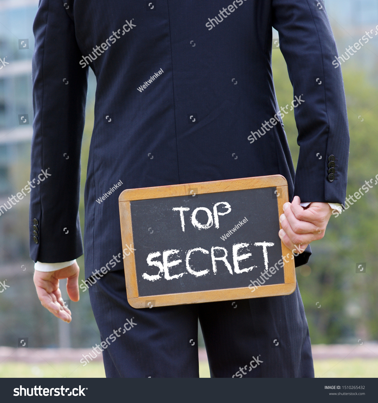 Business man holding a blackboard behind himself with the words Top Secret written with chalk #1510265432