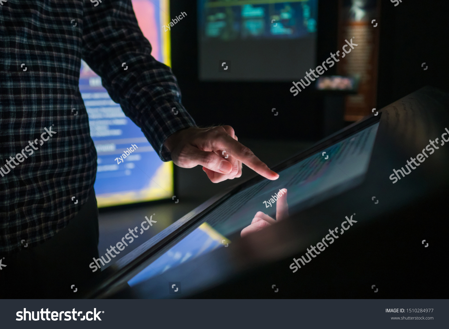 Man hand using interactive touchscreen display of electronic multimedia terminal at modern museum or exhibition. Evening time, low light illumination. Education, futuristic and technology concept #1510284977
