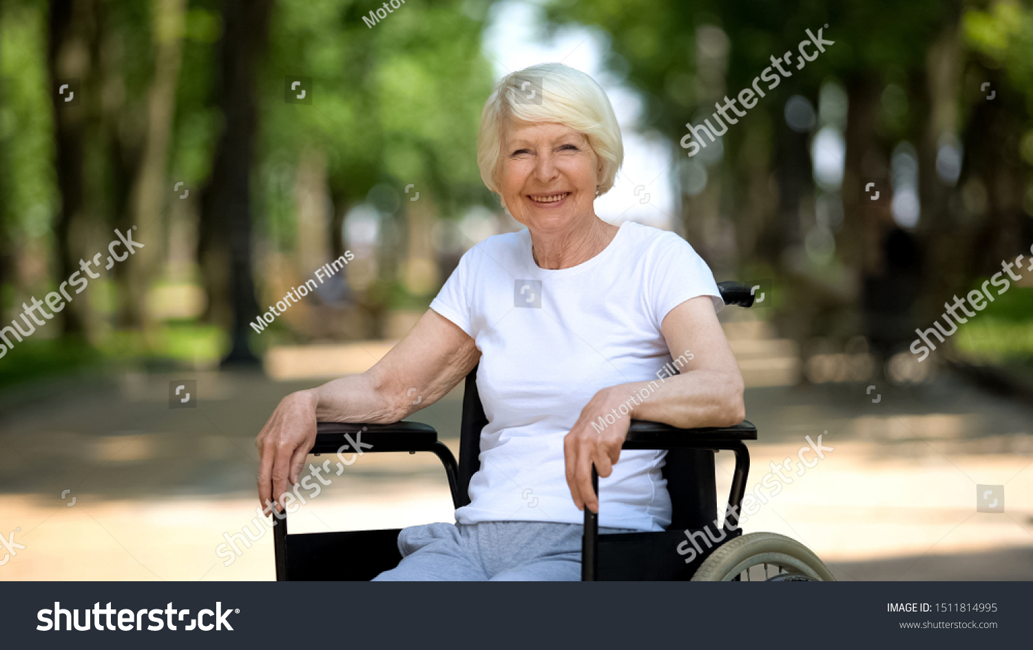 Smiling elderly woman in wheelchair looking into camera, sunny day in park #1511814995