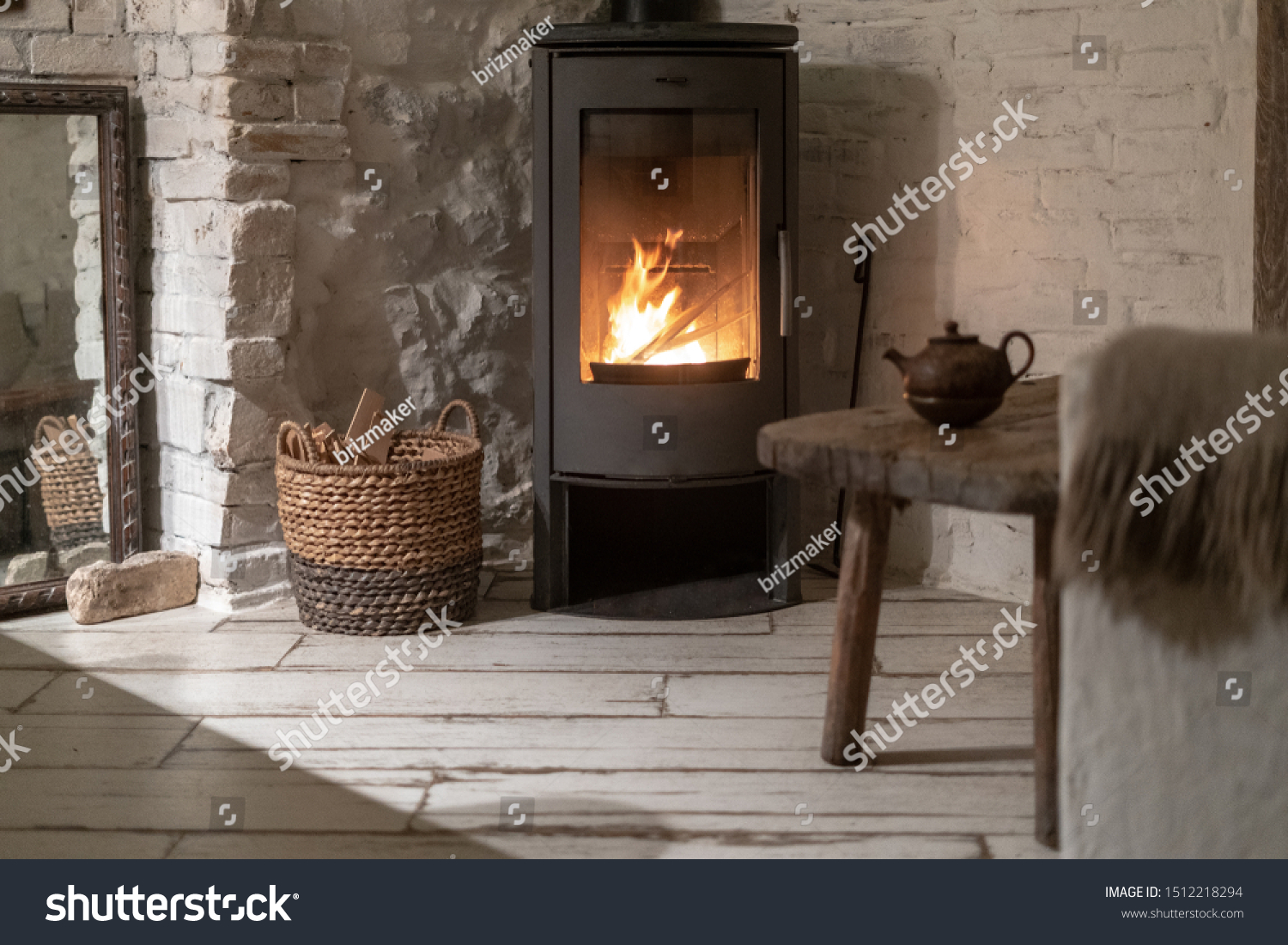 Wicker basket with firewood near fire chimney. Wood stove fireplace with metal body and glass door in comfort house with cozy interior in room #1512218294