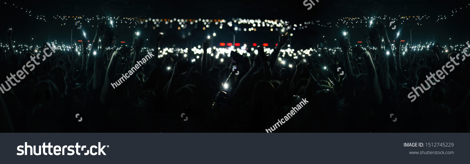 Wide concert crowd background. Large group of young people waving with mobile phone lights on a music festival #1512745229