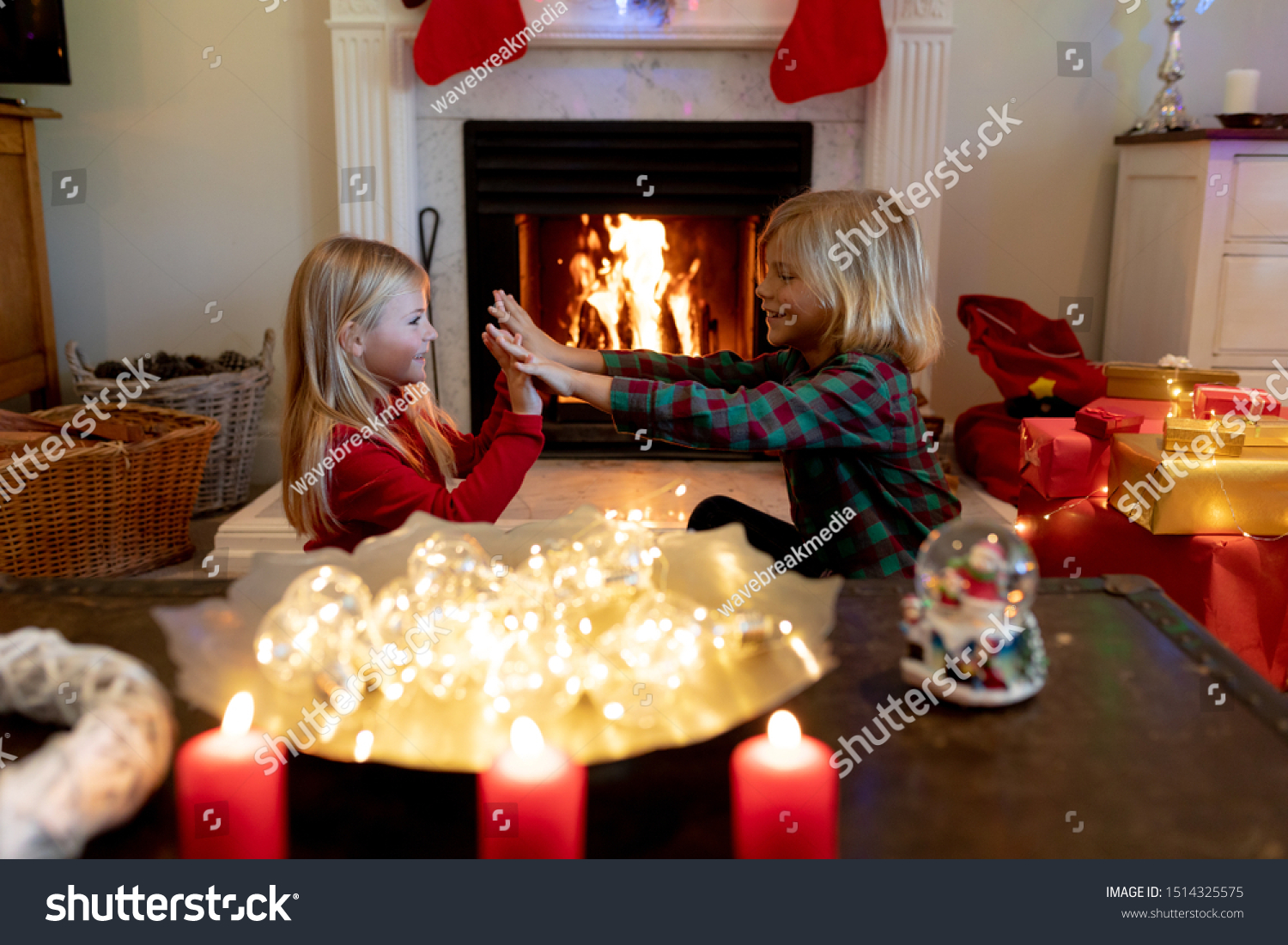 Side view of young Caucasian brother and sister sitting by the fireplace in their sitting room at Christmas time playing #1514325575