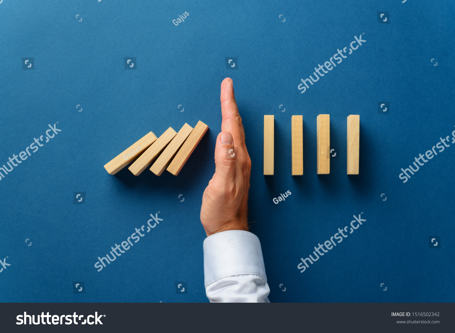 View from above of male hand interfering collapsing dominos in a conceptual image of business crisis management. Over navy blue background. #1516502342