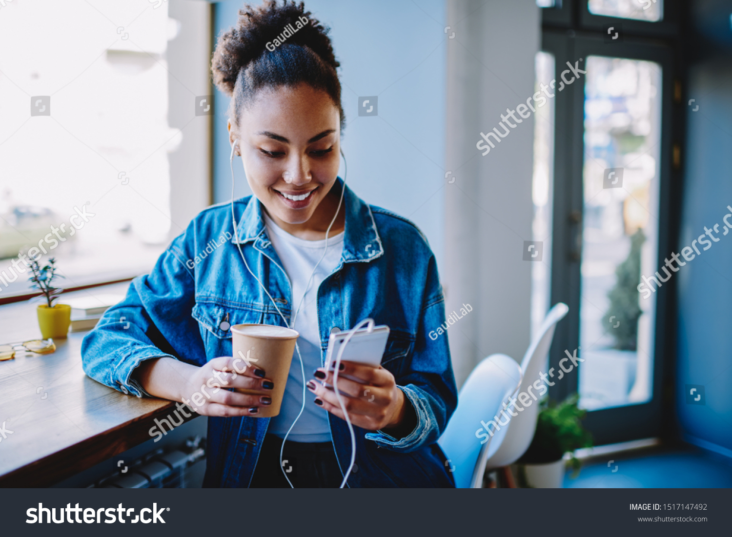 Happy female meloman typing name of song for search and download from multimedia application on cellular phone during coffee time in cafeteria,positive hipster girl listening audio book via headphones #1517147492