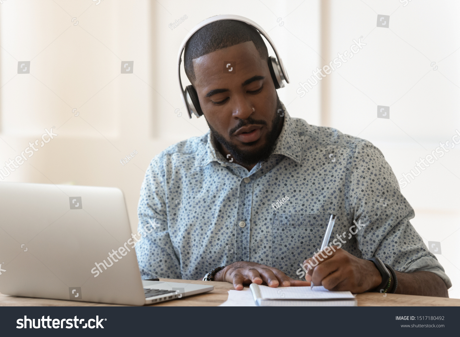 Focused african student sit at desk wearing wireless headphones learning preparing for seminar or exam, guy interpreter hears audio writing down translation, online lecture course e-learning concept #1517180492