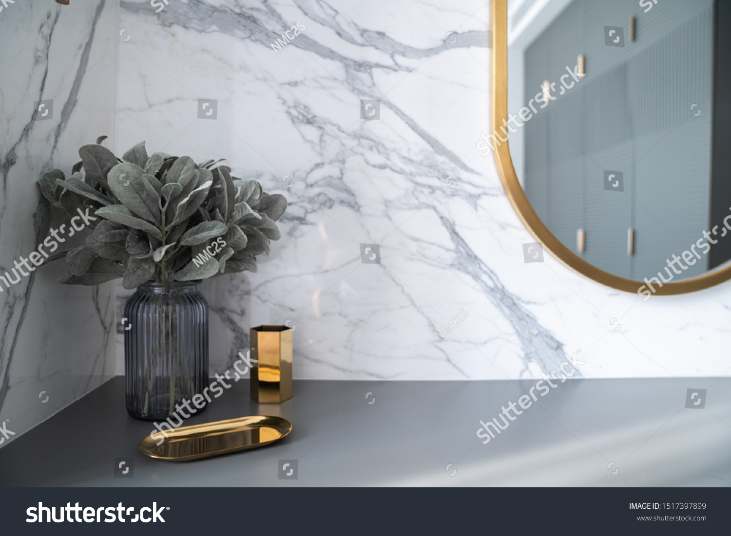 Bedroom working corner decorated with hexagon gold stainless vase and artificial plant in glass vase on gray spray-painted  working table with  marble wall in the background /apartment interior  #1517397899