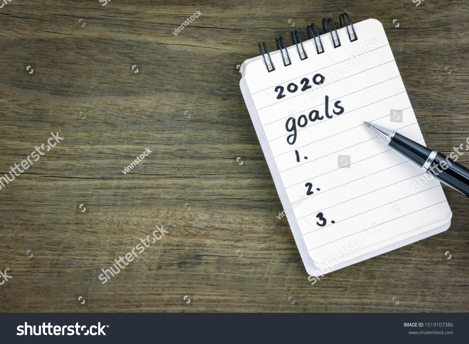 Top view 2020 goals list on notepad. Handwriting on memo paper notebook with black pen over wooden texture background, table blank space. Beginning of new goals and new year resolution concepts. #1519107386