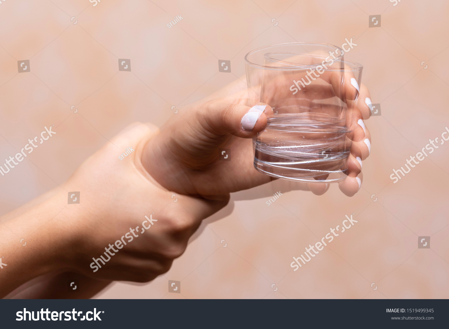 A closeup view on the hands of a person trying to hold a glass of water steady, shaking hands symptomatic of a central nervous and motor system disease such as Parkinson's #1519499345