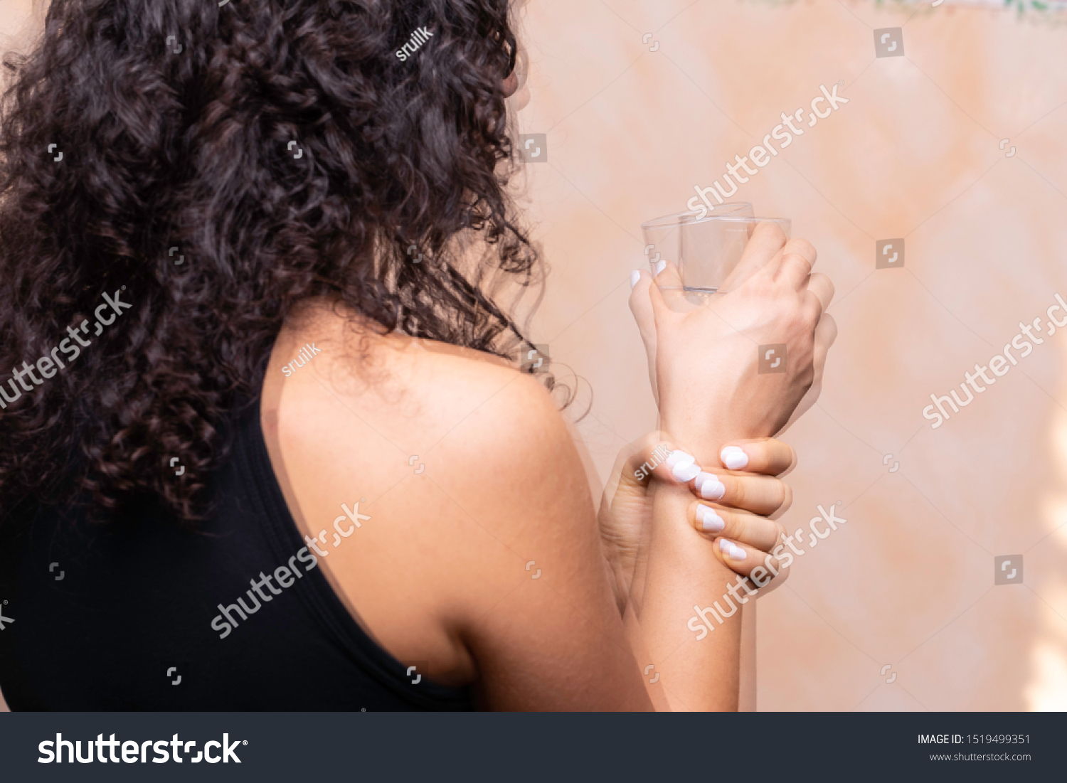 A closeup and rear view of a girl suffering from Parkinson's disease, violently trembling and holding her wrist trying to be steady, involuntary movements symptomatic of the disease. #1519499351