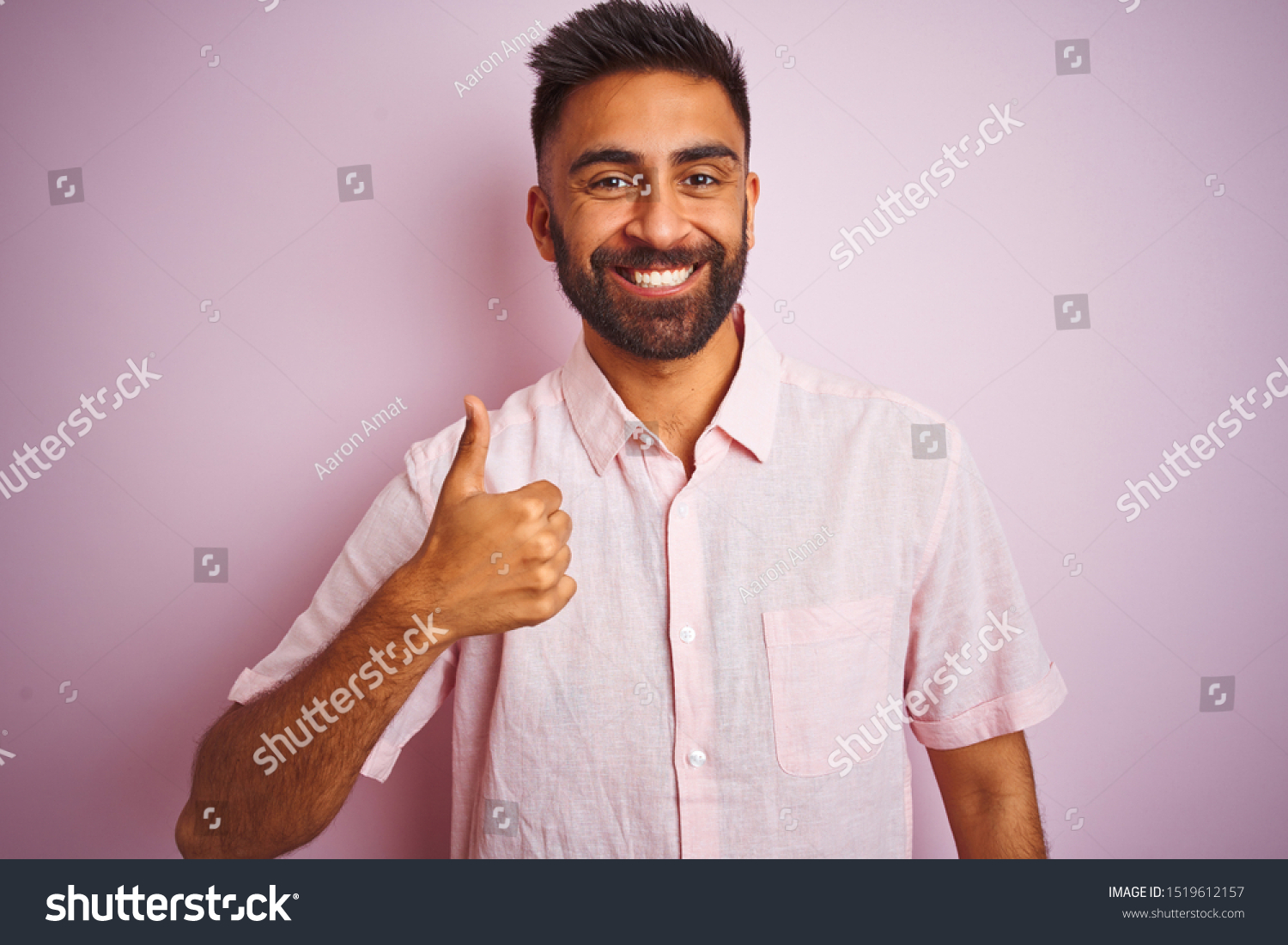 Young indian man wearing casual shirt standing over isolated pink background doing happy thumbs up gesture with hand. Approving expression looking at the camera showing success. #1519612157