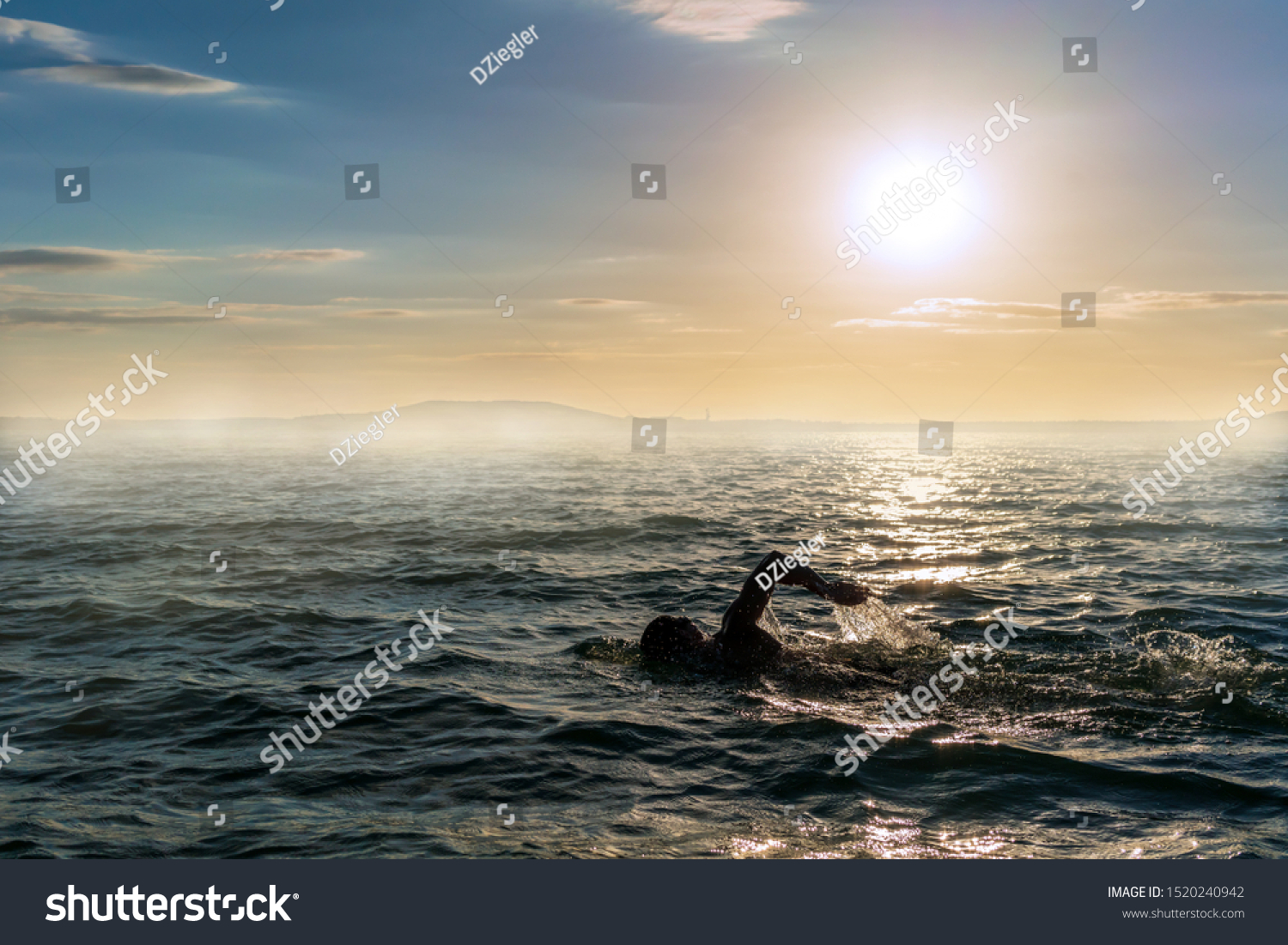 Man swimming in open water during a misty sunset #1520240942